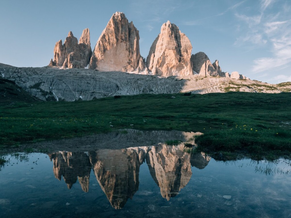Tre Cime di Lavaredo pale peaks reflected in a still alpine pool at golden hour