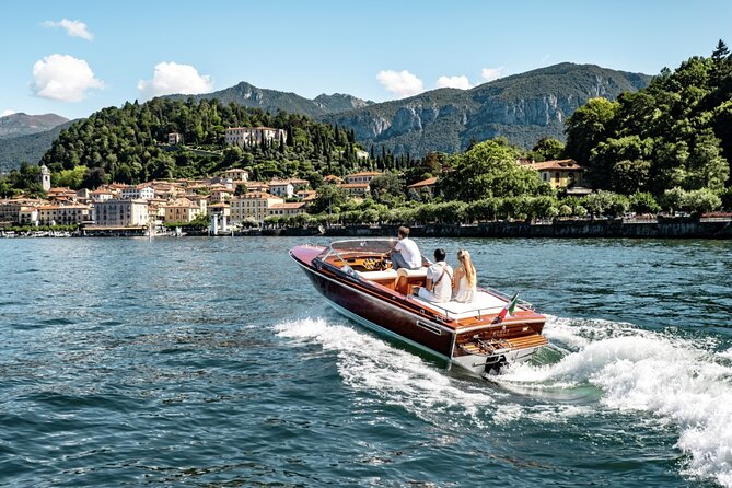 Classic wooden motorboat on Lake Como with guests, white wake, villas and green hills along the shore