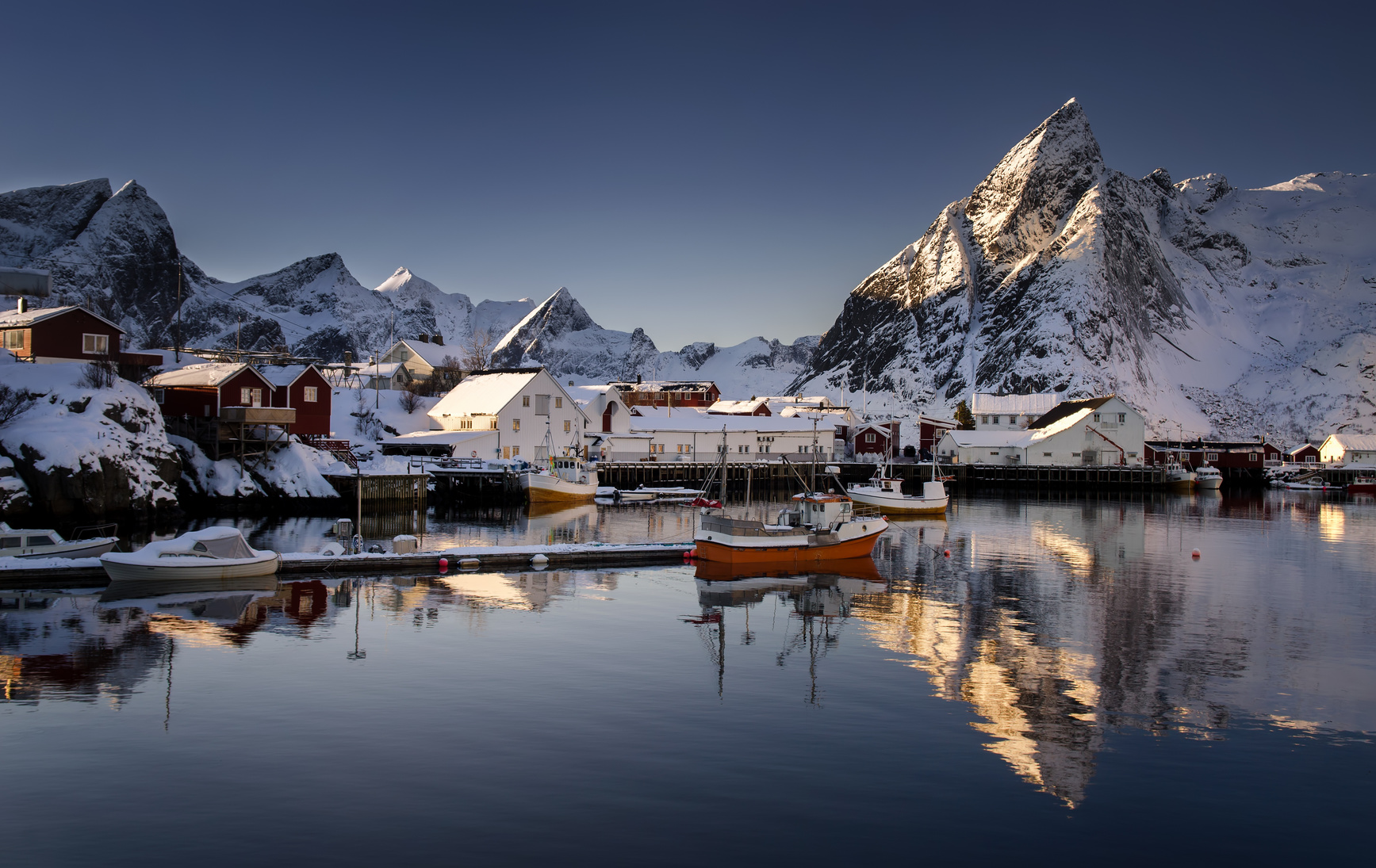 Fishing village and fjord below sharp snow-covered mountains
